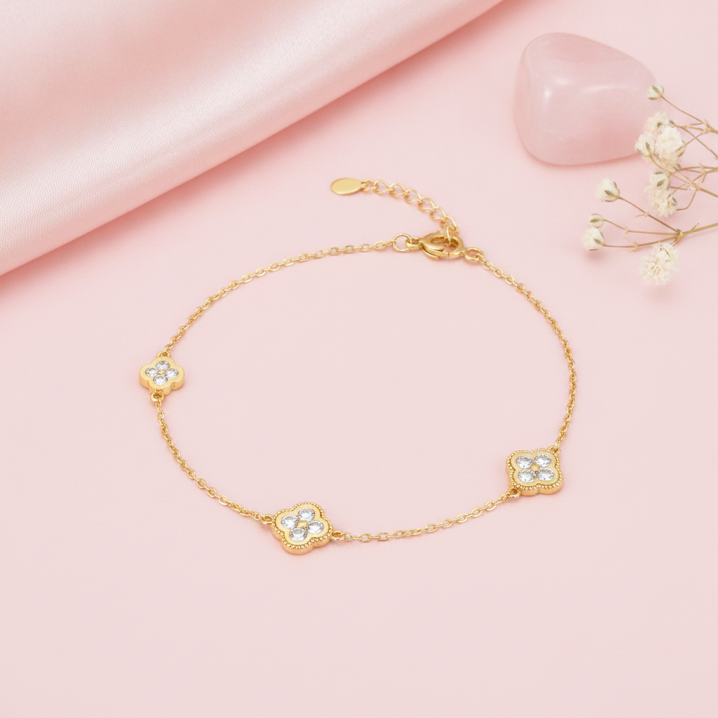 gold clover charm bracelet with White CZ stones, styled with a pink stone and dried flowers on a blush background