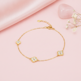 gold clover charm bracelet with White CZ stones, styled with a pink stone and dried flowers on a blush background
