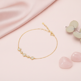 gold clover and round link station bracelet with White CZ stones, styled with rose quartz stones and eucalyptus leaves on a blush background