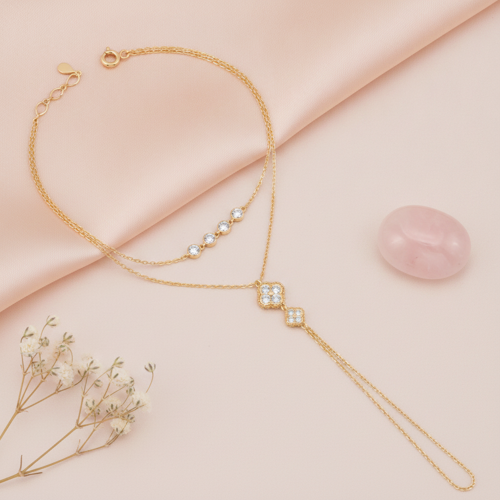 gold hand chain bracelet with bezel-set stones and a floral motif drop, styled with a rose quartz stone on a blush background