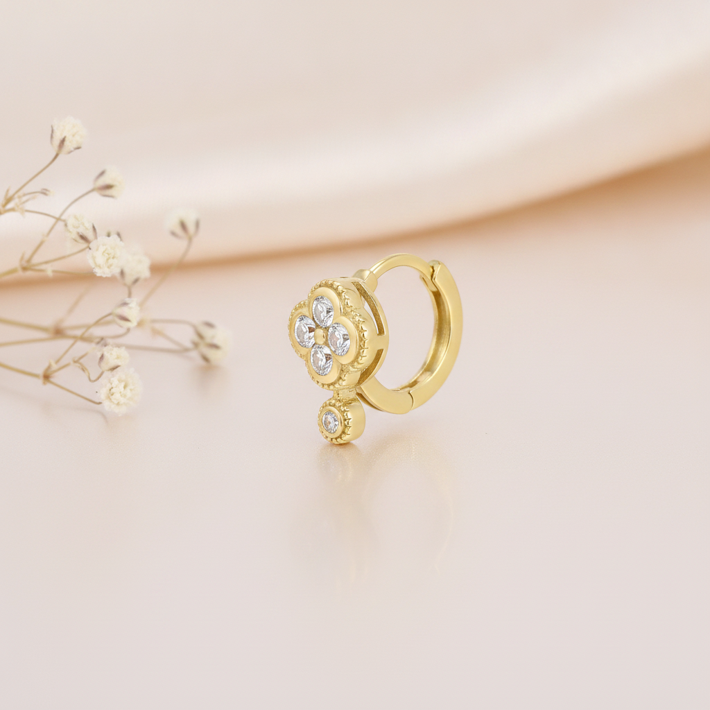 gold huggie hoop earring with a beaded clover motif and White CZ stones, styled with dried flowers on a blush background