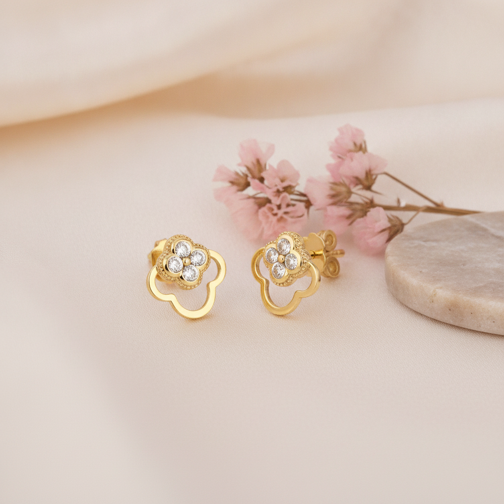 pair of gold open clover stud earrings with White CZ stones, styled with pink flowers on a cream background