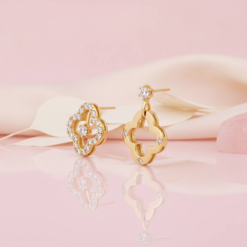 pair of asymmetric gold clover earrings with pave and solitaire stones, styled with a rose quartz stone on a blush background