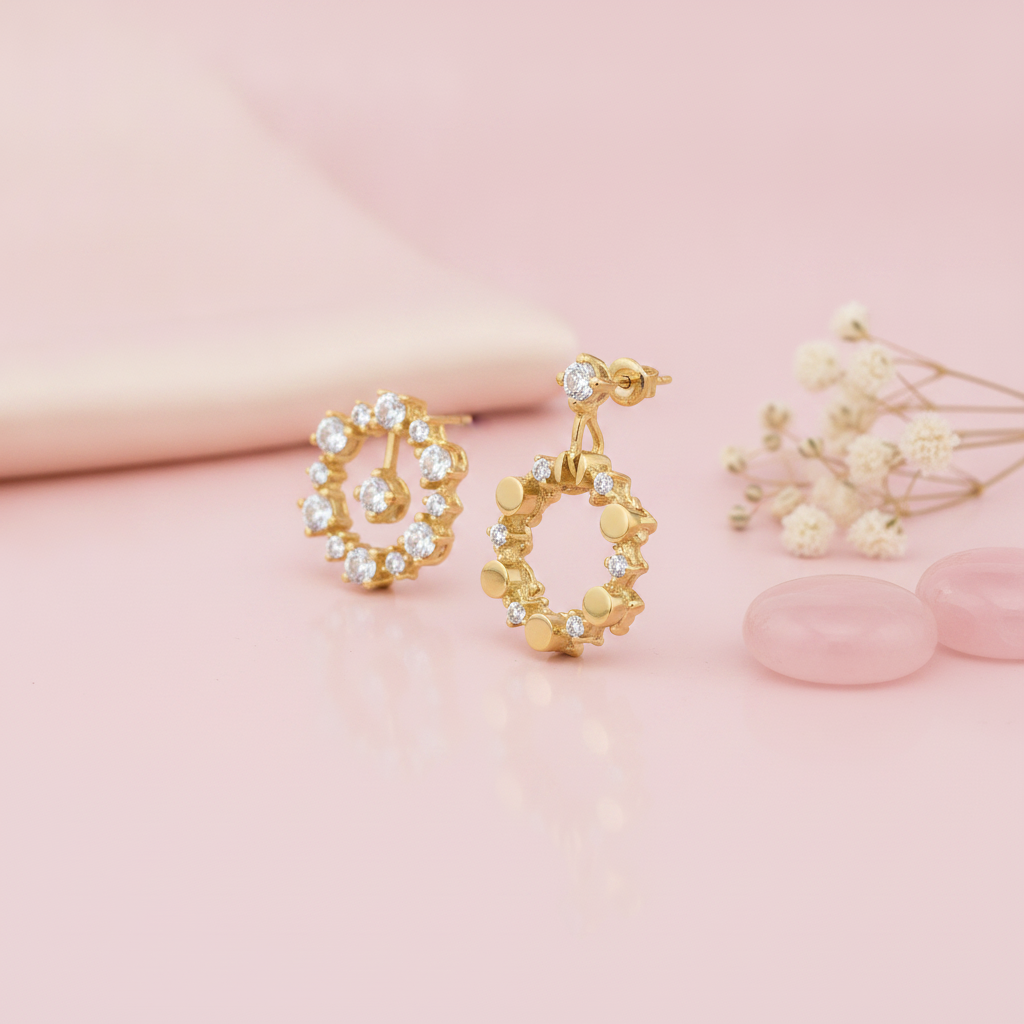 pair of asymmetric gold halo earrings with White CZ stones and polished gold discs on a blush background