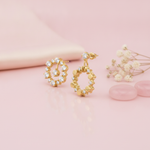 pair of asymmetric gold halo earrings with White CZ stones and polished gold discs on a blush background