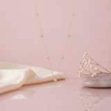 Gold station necklace with clover-shaped stone motifs suspended against a pink background with dried flowers