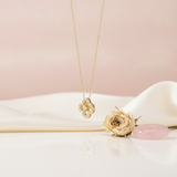 Gold open clover pendant necklace with a suspended center stone on a pink background with a dried rose