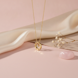 Gold circle pendant necklace with pave stones and a suspended center stone on a pink background with a stone prop