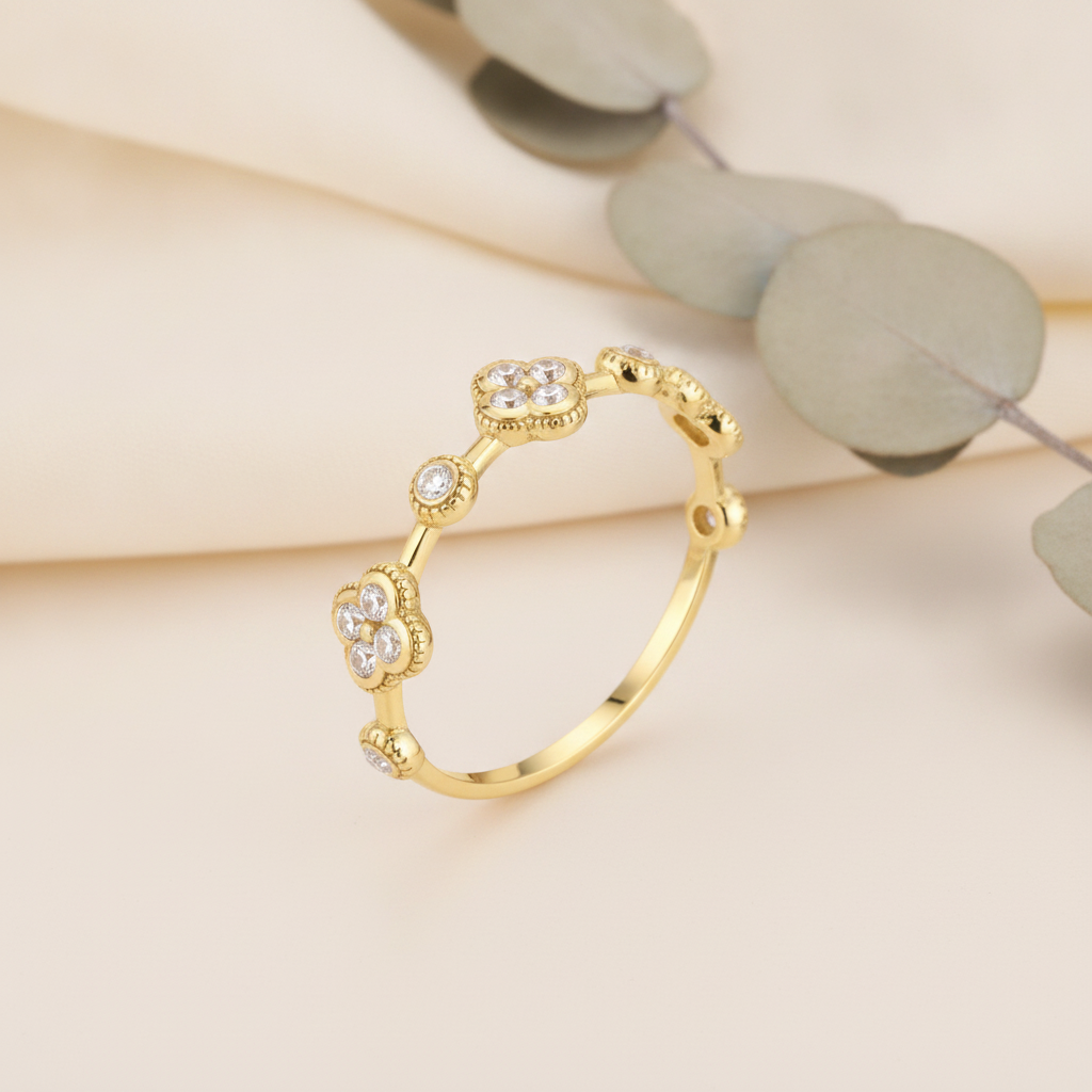 Gold ring with alternating clover motifs and framed stones on a neutral background with eucalyptus leaves