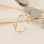 Gold ring with alternating clover motifs and framed stones on a neutral background with eucalyptus leaves