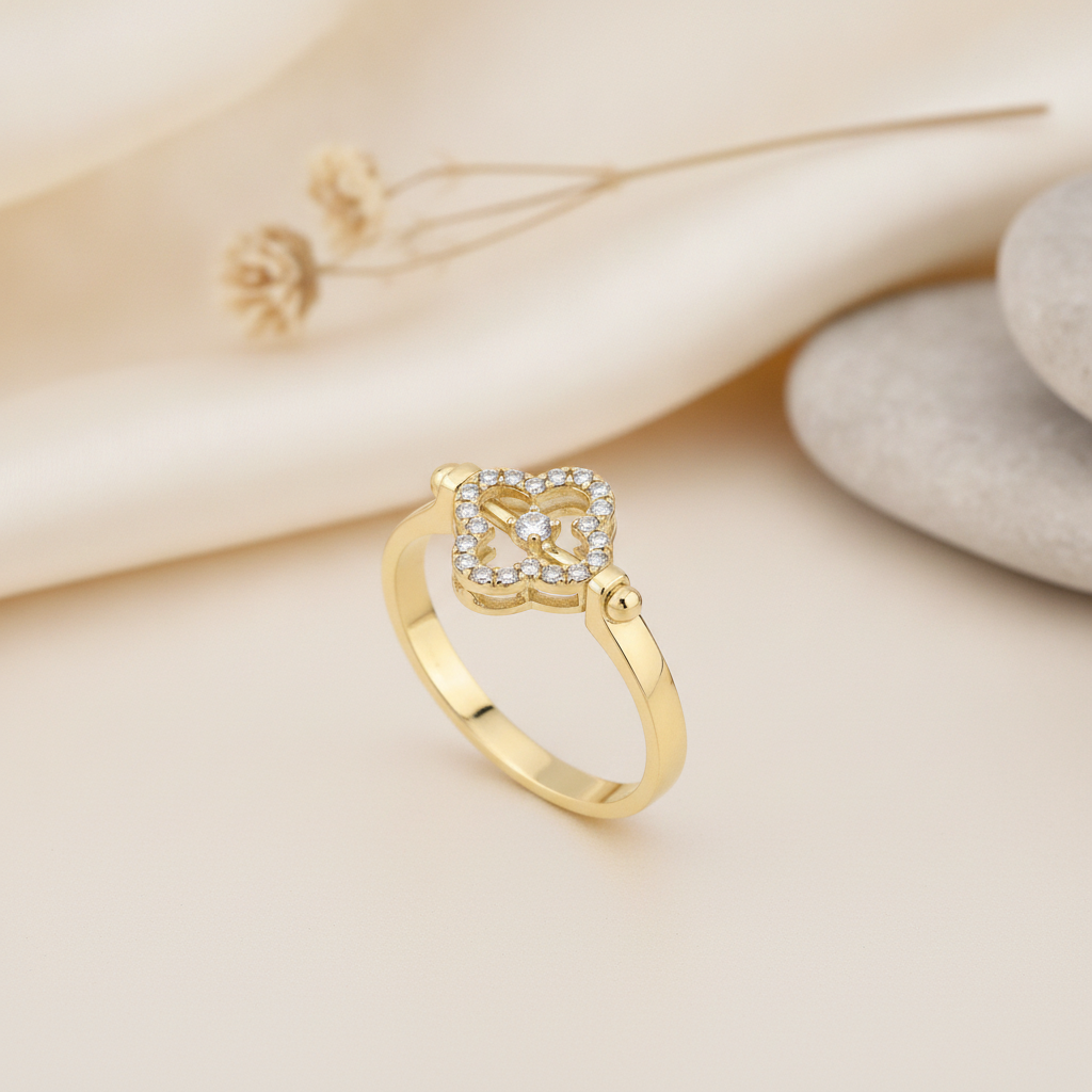 yellow gold ring with an open quatrefoil motif of pave stones and a center stone, styled on cream fabric with a dried flower and stacked pebbles