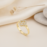 yellow gold ring with an open quatrefoil motif of pave stones and a center stone, styled on cream fabric with a dried flower and stacked pebbles