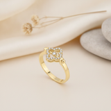 yellow gold ring with an open quatrefoil motif of pave stones and a center stone, styled on cream fabric with a dried flower and stacked pebbles