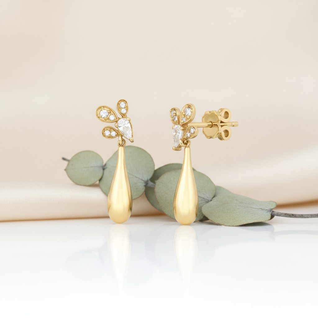 yellow gold petal drop earrings with a pear-cut stone and a long teardrop, styled with a eucalyptus sprig on a cream background