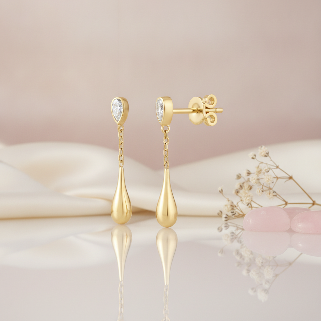 yellow gold chain teardrop earrings with a pear-cut bezel stud, styled on cream silk with pink stones