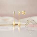 yellow gold chain teardrop earrings with a pear-cut bezel stud, styled on cream silk with pink stones