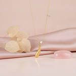 yellow gold curved teardrop pendant necklace with a marquise stone, styled on cream silk with dried leaves and a rose quartz stone