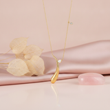 yellow gold curved teardrop pendant necklace with a marquise stone, styled on cream silk with dried leaves and a rose quartz stone