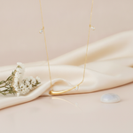 yellow gold horizontal teardrop bar necklace with pear-cut stones, styled on cream silk with dried flowers and a translucent stone