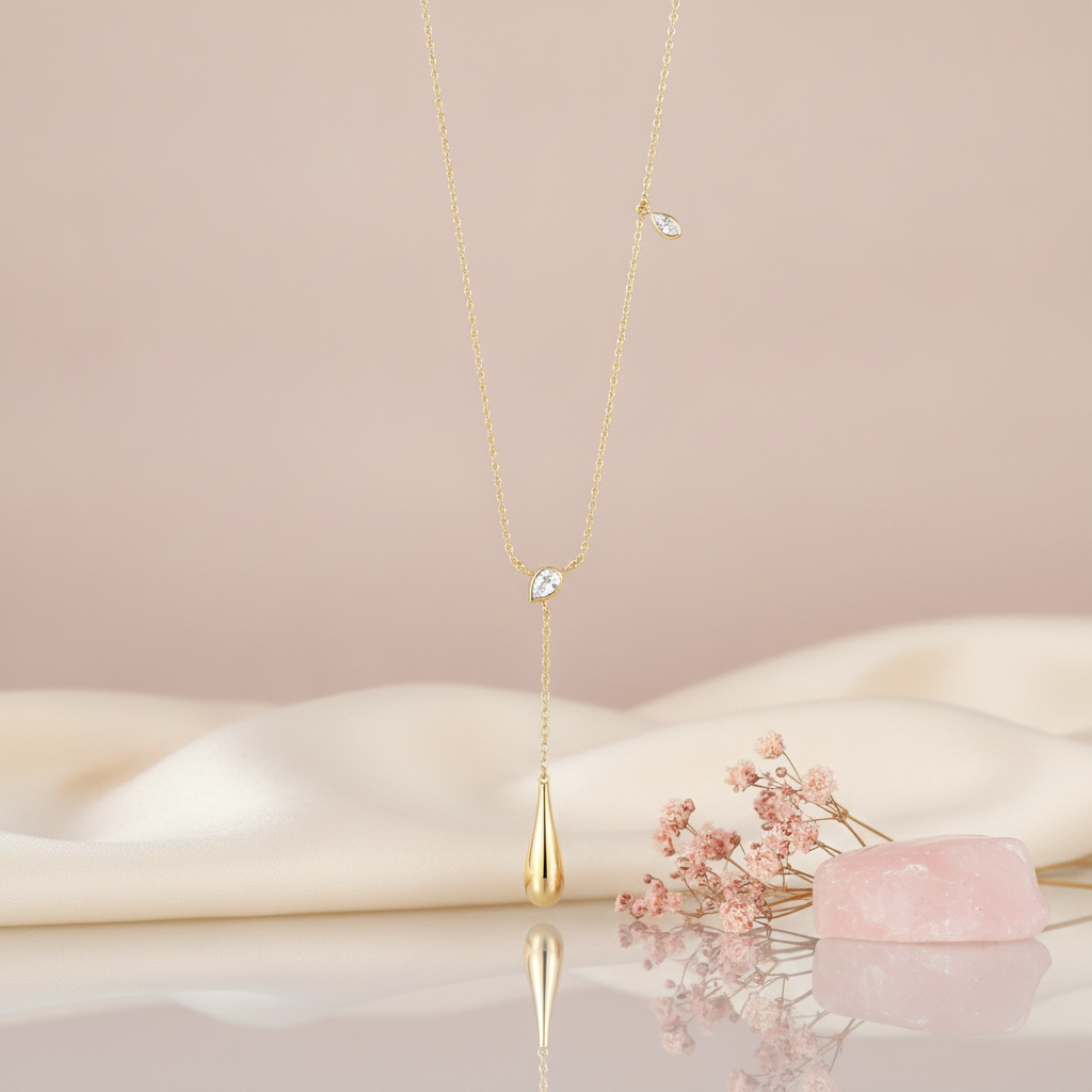 yellow gold lariat necklace with a pear-cut stone and a polished teardrop drop, styled on a pink background with dried baby's breath and a rose quartz stone