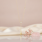 yellow gold lariat necklace with a pear-cut stone and a polished teardrop drop, styled on a pink background with dried baby's breath and a rose quartz stone