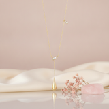 yellow gold lariat necklace with a pear-cut stone and a polished teardrop drop, styled on a pink background with dried baby's breath and a rose quartz stone