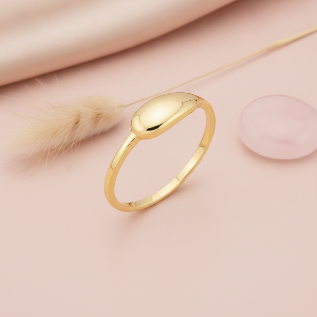 yellow gold ring with a smooth raised oval dome, styled on a pink background with a dried pampas grass sprig and a rose quartz stone