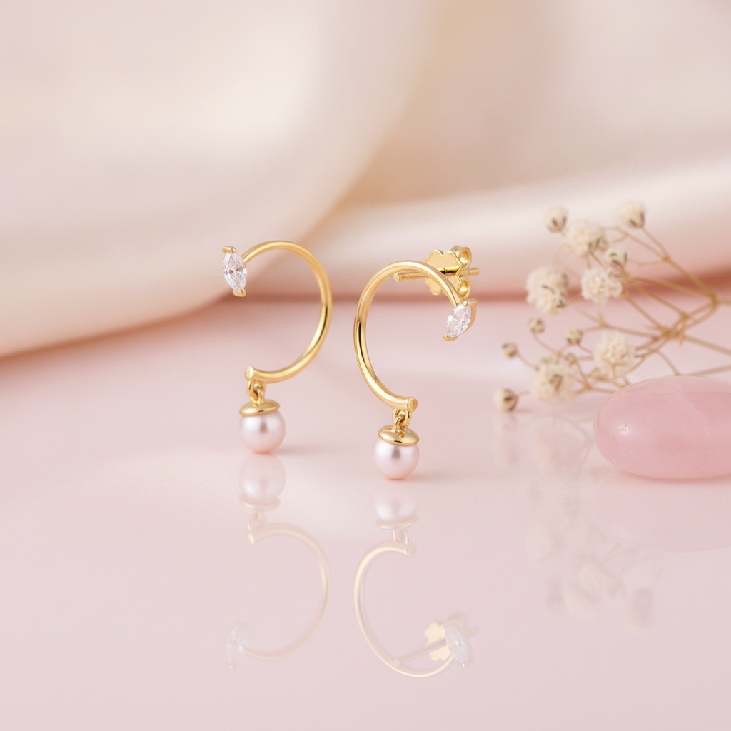 yellow gold open hoop earrings with a marquise stone and a dangling pearl, styled on a pink background with dried baby's breath and rose quartz stones