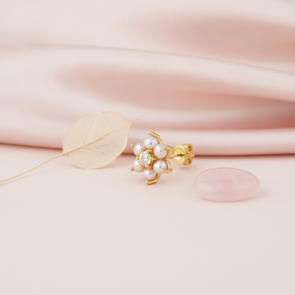 yellow gold floral stud earring with pearls and a clear stone, styled on pink silk with a dried leaf and a rose quartz stone
