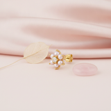 yellow gold floral stud earring with pearls and a clear stone, styled on pink silk with a dried leaf and a rose quartz stone