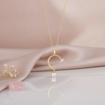 yellow gold open arc pendant necklace with a marquise stone and a dangling pearl, styled on cream silk with dried baby's breath and a rose quartz stone