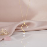 yellow gold open arc pendant necklace with a marquise stone and a dangling pearl, styled on cream silk with dried baby's breath and a rose quartz stone