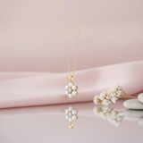 yellow gold floral pendant necklace with pearls and a clear stone, styled on pink silk with dried baby's breath and pebbles