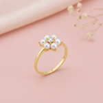 yellow gold floral ring with pearls and a clear stone, styled on a pink background with dried baby's breath