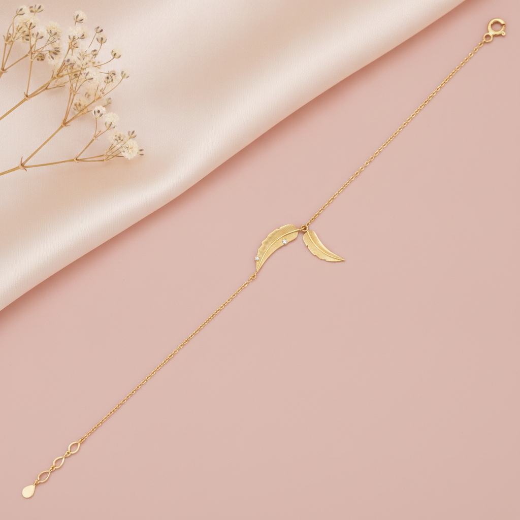 yellow gold feather chain bracelet with two textured feathers, styled on a pink background with dried baby's breath
