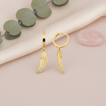 yellow gold huggie hoop earrings with textured feather drops, styled on cream fabric with eucalyptus leaves and a rose quartz stone