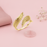 yellow gold open wrap ring with two textured feathers and accent stones, styled on a pink background with dried baby's breath and a rose quartz stone
