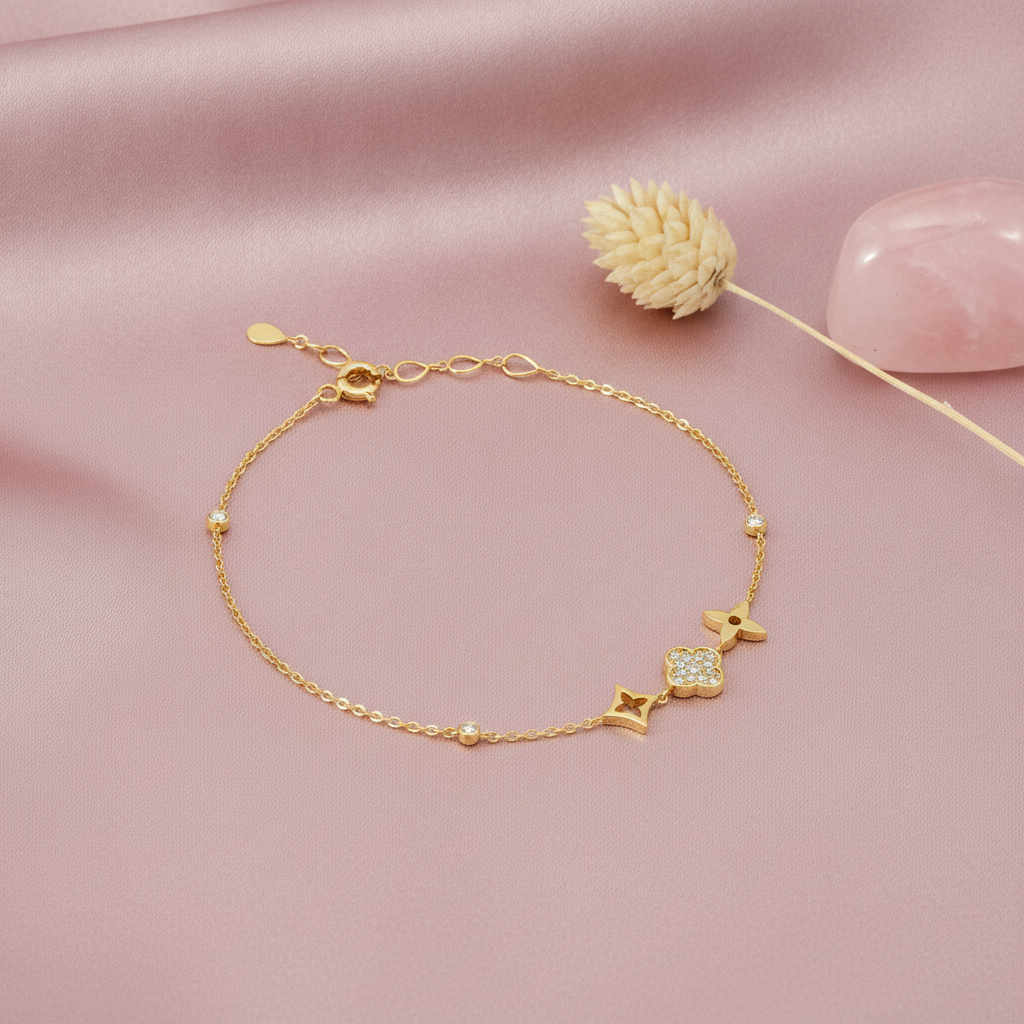 yellow gold charm bracelet with star, clover, and floral motifs, styled on a pink background with a dried flower and rose quartz stones