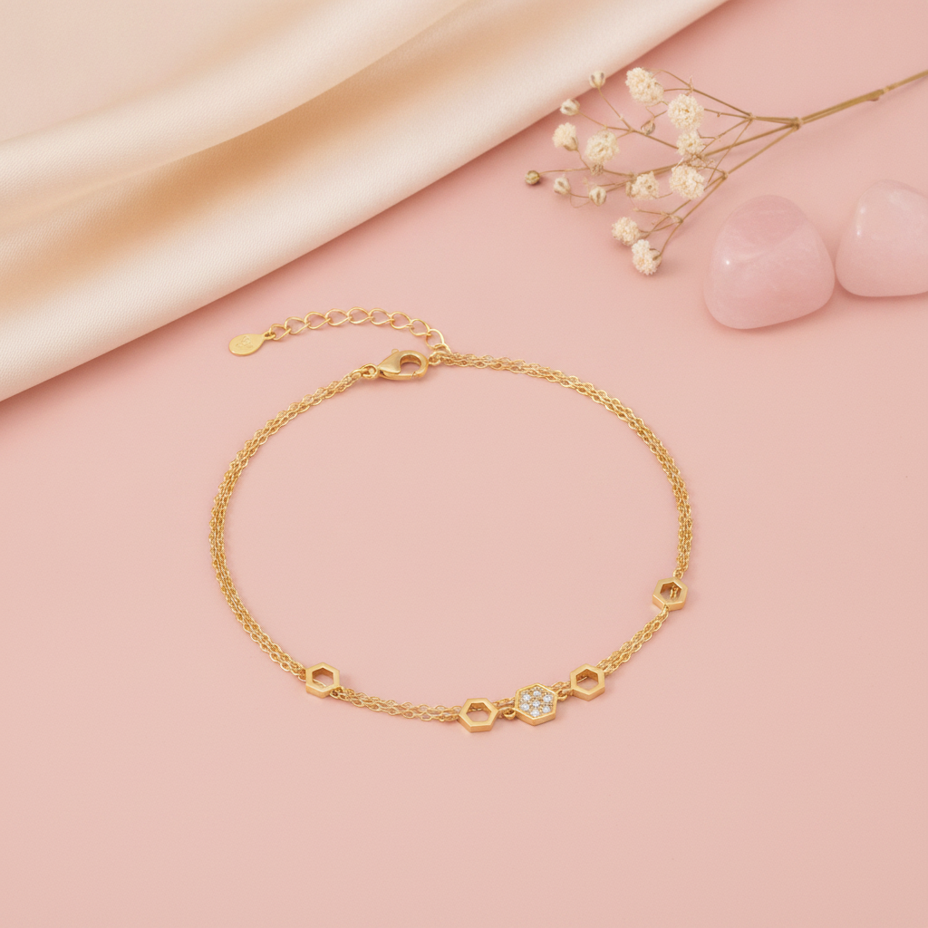 yellow gold double-strand hexagon bracelet with a honeycomb motif, styled on a pink background with dried baby's breath and rose quartz stones