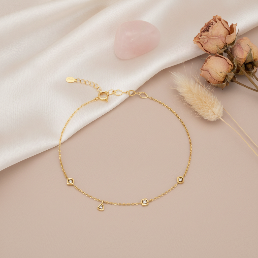 gold bracelet with square and trillion bezel-set stone stations, shown on cream fabric with a rose quartz stone and dried roses