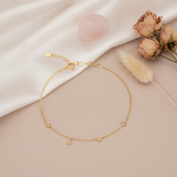 gold bracelet with square and trillion bezel-set stone stations, shown on cream fabric with a rose quartz stone and dried roses