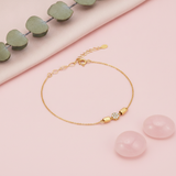 gold bracelet with a pave disc charm flanked by polished capsule beads, shown on pink fabric with eucalyptus leaves and rose quartz stones