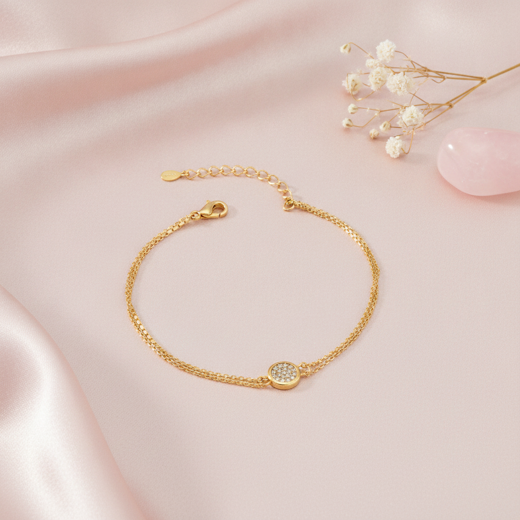 gold bracelet with a pave-set circular disc charm between a single and double chain, shown on pink fabric with baby's breath and a rose quartz stone
