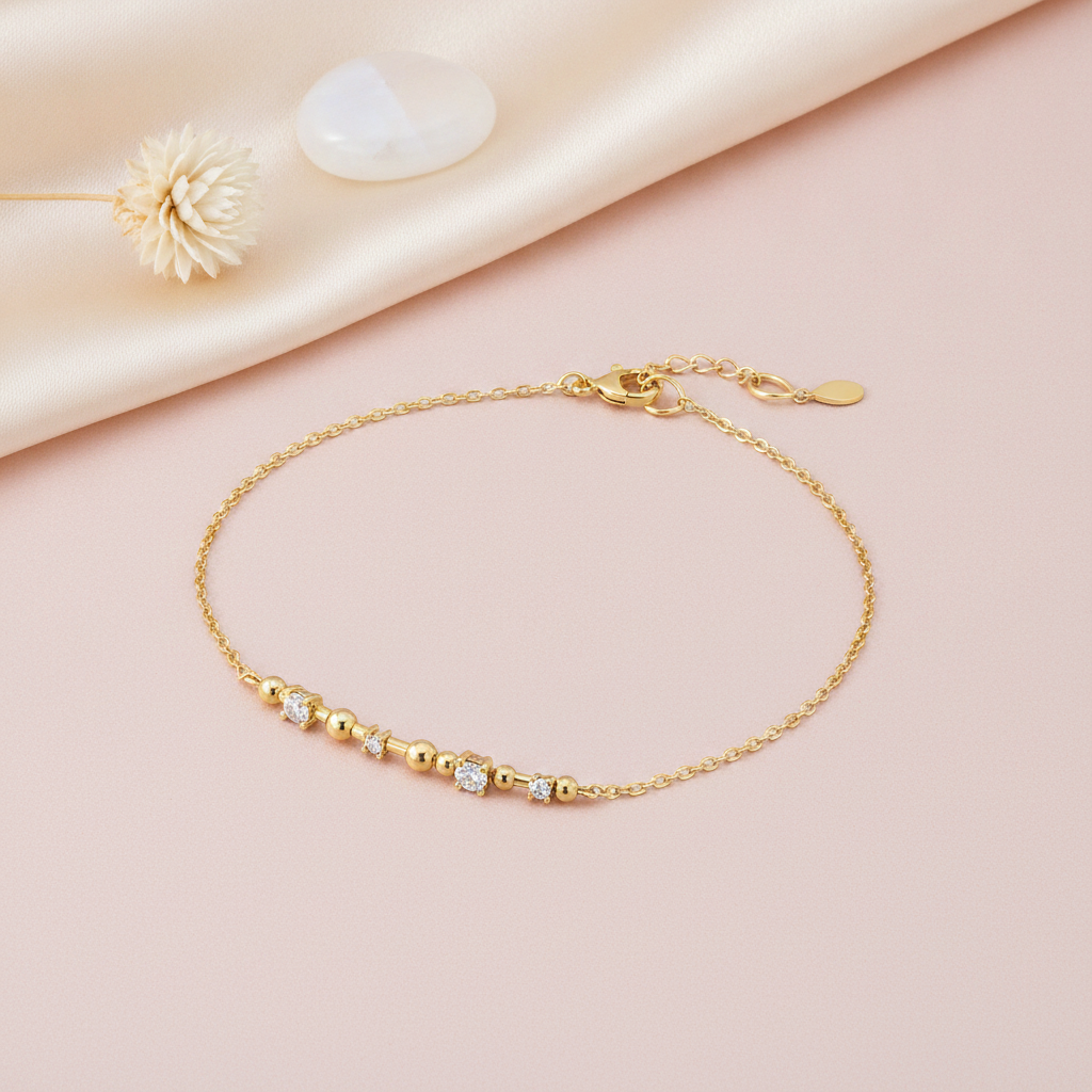gold bracelet with alternating polished gold beads and small stone accents, shown on pink fabric with a dried flower and a smooth stone