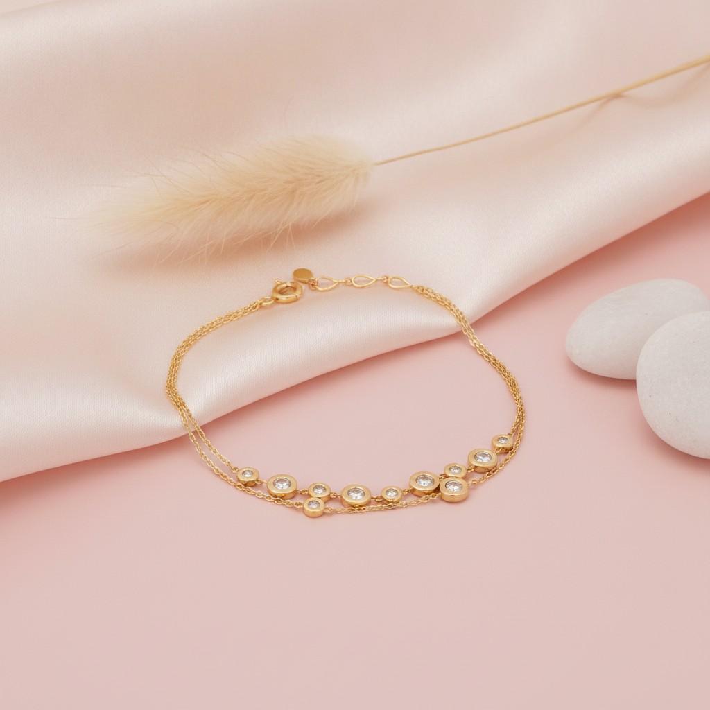 double strand gold bracelet with scattered bezel-set stone circles, shown on pink fabric with a dried plume and smooth pebbles