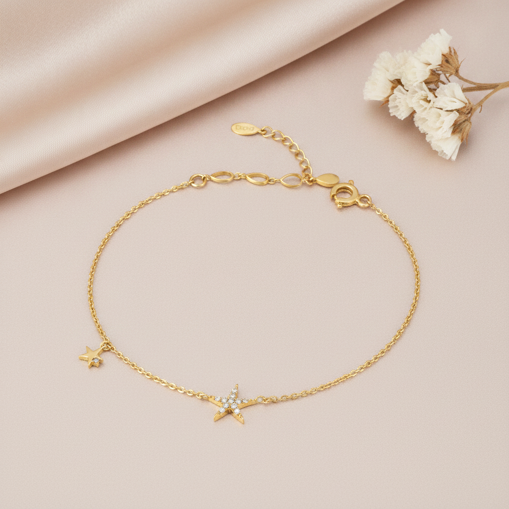 gold bracelet with a stone-set star charm and a smaller star charm, shown on tan fabric with dried flowers
