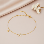 gold bracelet with a stone-set star charm and a smaller star charm, shown on tan fabric with dried flowers
