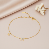 gold bracelet with a stone-set star charm and a smaller star charm, shown on tan fabric with dried flowers