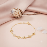 gold chain bracelet with clover clusters set with clear stones, on pink fabric with a dried protea flower