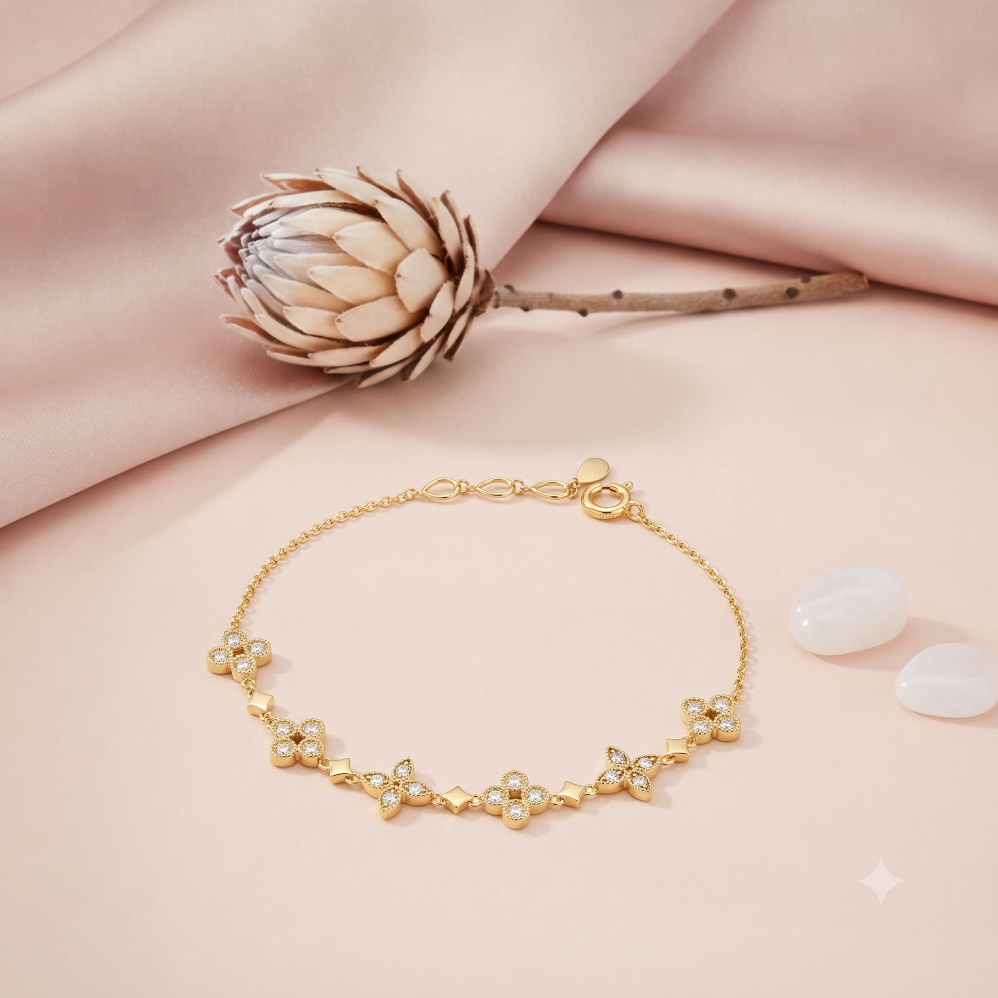 gold chain bracelet with clover clusters set with clear stones, on pink fabric with a dried protea flower